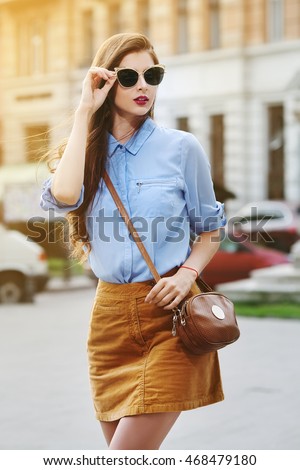 Female fashion concept. Outdoor portrait of young beautiful confident lady walking on the street. Model wearing stylish clothes and sunglasses. Girl looking aside. Sunny day. City lifestyle. Waist up Royalty-Free Stock Photo #468479180