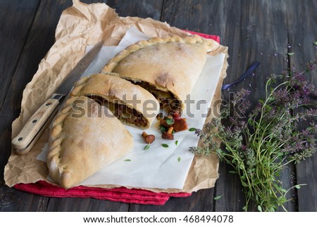 Italian pizza calzone with mushrooms, spinach and cheese on a wooden surface with a bunch of thyme, rustic style, selective focus