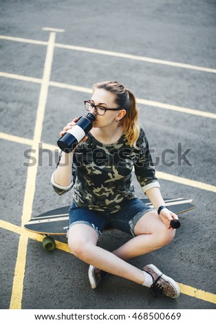 Young girl sitting on a longboard and drinks water from a metal bottle