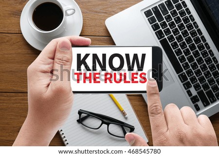 KNOW THE RULES message on hand holding to touch a phone, top view, table computer coffee and book