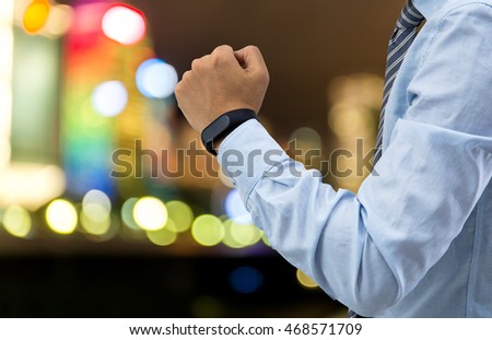 isolated business man with smart wristband and smartphone on city light background
