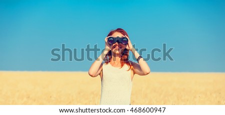 photo of the beautiful young woman with binocular standing in the field