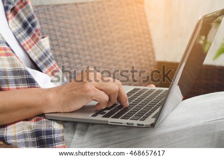 A man in casual wear sits on arm chair using laptop computer at home in relax position.