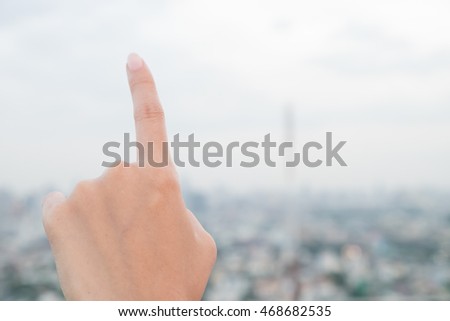 a woman show left side hand show forefinger/index finger, correct, pointing, shoot, point up with blur building in the city background
