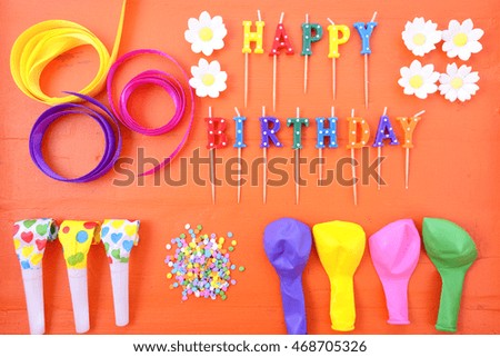 Happy Birthday flat lay with party decorations on a bright orange wood table. 