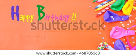 Happy Birthday background with party decorations on a bright orange wood table, sized to fit a popular social media cover image placeholder.