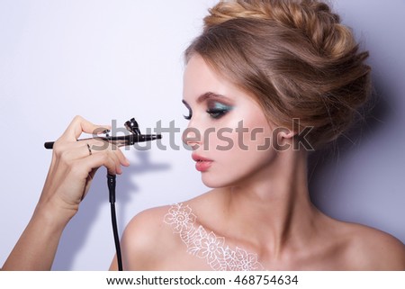 Beauty Fashion Model Woman , portrait,  hairstyle with braids. Concept Girl face with perfect skin in bright Background with hand holding aerograph. Mehndi , white henna tattoo on shoulders. Royalty-Free Stock Photo #468754634