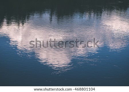 calm river in forest with reflections and trees on both sides of the stream - vintage film effect