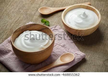 Greek yogurt in a wooden bowl with spoons on wooden background