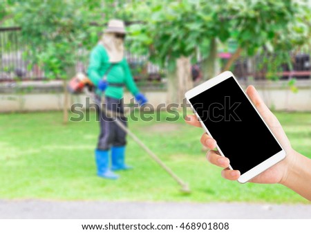 woman use mobile phone and blurred image of a man use a lawnmower in the yard