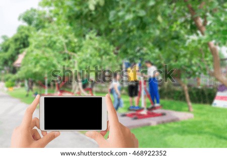 woman use mobile phone and blurred image of the girls play with exercise equipment in the park