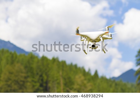 White drone quad copter with high resolution digital camera flying in the blue sky over the mountain