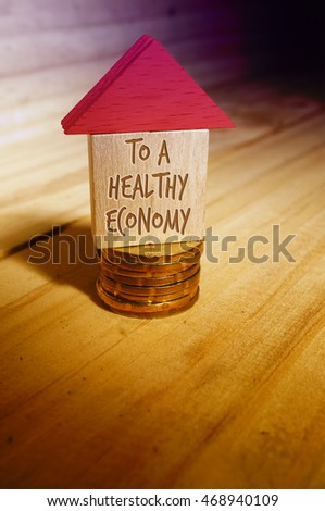 Arrow Direction the way to a healthy economy. Wooden House with stack of coins and blur background