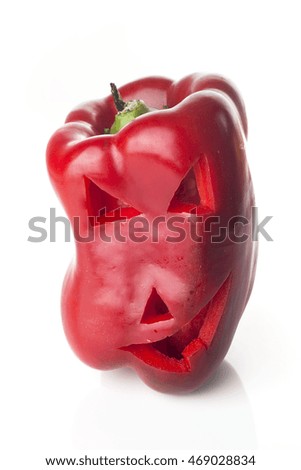 Food art creative concept. Halloween scary face carved into red capsicum vegetables isolated over a white background.
