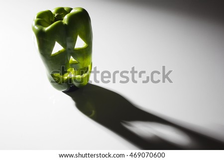 Food art creative concept. Halloween scary face carved into green capsicum vegetables  with back light over a dark background and shadows. Text space.