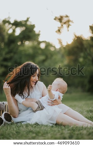 Happy young mother having fun, bowl, rising up, piggyback ride her child in park on summer sunset