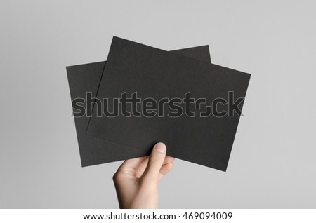 Black A5 Flyer / Invitation Mock-Up - Male hands holding black flyers on a gray background.