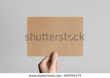 Kraft A5 Flyer / Invitation Mock-Up - Male hands holding a kraft flyer on a gray background.