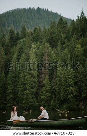 Vintage wedding photography of a young hipster couple curly bride posing in a boat at sunset in the forest and mountains dressed in a suite and white dress 
