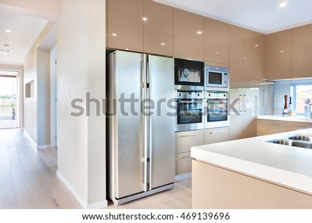 Expensive and modern kitchenware including silver color and tall two door refrigerator and four ovens and stoves fixed to the wall with cabinets around it. There is a ceramic counter top with the sink Royalty-Free Stock Photo #469139696