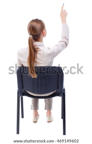 back view of young beautiful  woman sitting on chair and pointing.  girl  watching. Rear view people collection. Skinny girl in white denim suit sitting on an office chair and shows up finger.