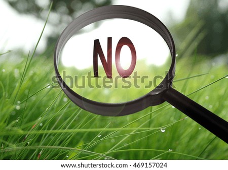 Magnifying glass with the word no on grass background. Selective focus
