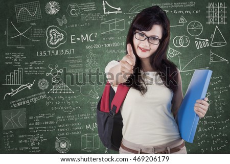 Photo of a female college student showing OK sign in the class with scribble on the chalkboard