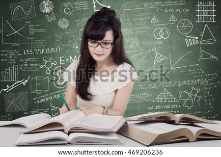 Photo of a pretty female high school student learning in the class while writing and reading books