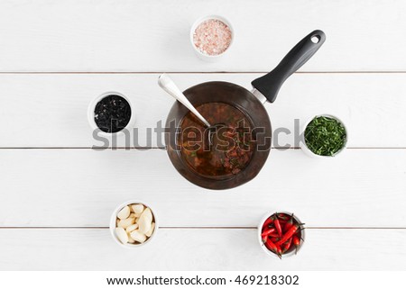 Cooking sauce for seafood, white wooden background. Tasty gravy in pan with spoon on table with variety of ingridients. Mediterranean cuisine, lusury restaurant food