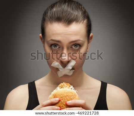 Diet concept: woman holding burger with mouth sealed