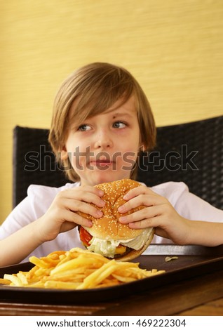 cute blond boy eating a hamburger and fries