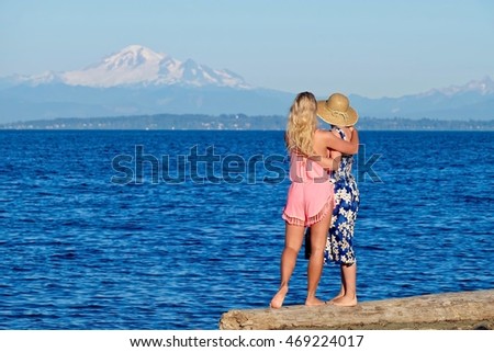 Grown up family of two. Mother and daughter hugging on beach by blue sea. Centennial Beach at Boundary Bay Regional Park, Tsawwassen, British Columbia, Canada. 