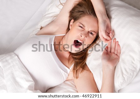 Young woman lies in bed and yawning