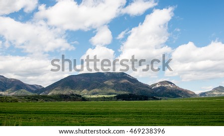 Dark storm clouds over meadow with green grass and mountains in background