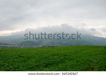 Dark storm clouds over meadow with green grass and mountains in background