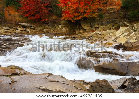 Mountain fast flowing river stream of water in the rocks with blue sky at autumn time. Colorfull foliage