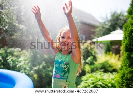 Preschooler cute girl playing with garden sprinkler. Summer outdoor water fun in the backyard