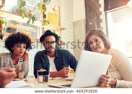 Portrait of creative people sitting at a coffee shop and looking at laptop. Business team discussing new project ideas at a cafe.