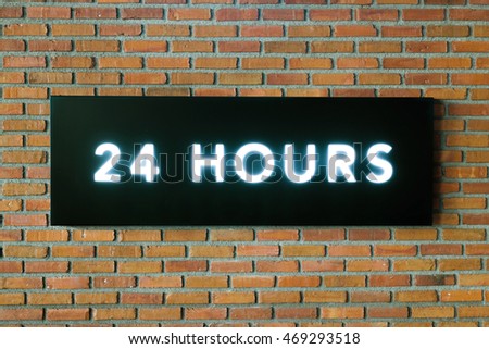 Twenty four hours glowing sign on black board and brick wall