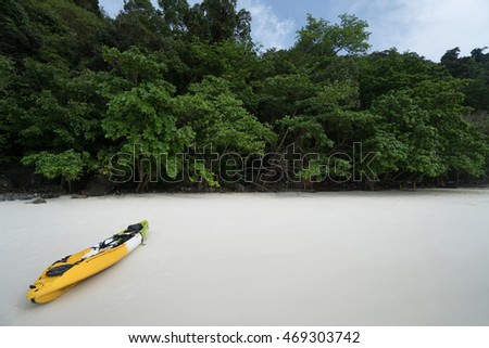 A yellow kayak on a tropical beach over green trees background