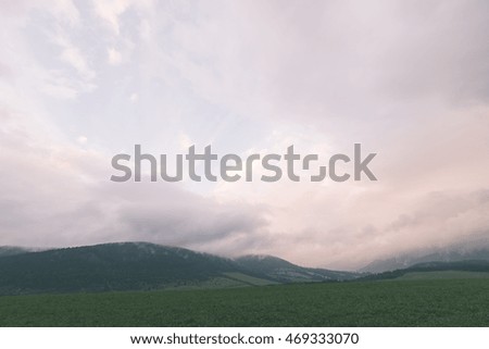 Dark storm clouds over meadow with green grass and mountains in background - vintage effect