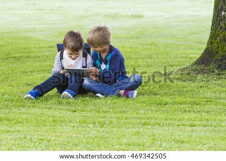 Little boys sitting on the grass in a park and using tablet PC. Technology, lifestyle, education, people concept