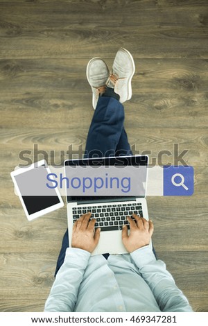 Young man sitting on floor with laptop and searching SHOPPING concept on screen
