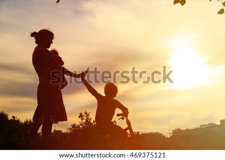 Silhouette of mother with little baby and son on bike