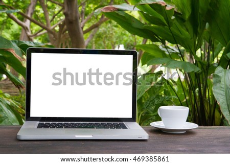 Conceptual workspace, Laptop with blank screen on table,coffee cup and green garden background,business technology concept