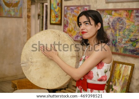 A beautiful mysterious girl is playing a tambourine against the colorful background