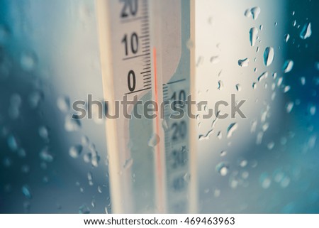 Closeup photo of household alcohol thermometer showing temperature in degrees Celsius with rain drops on glass. Cold weather and forecast concept. Toned picture