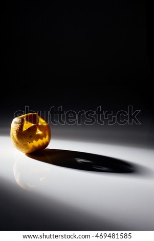 Food art creative concept. Halloween scary face carved into yellow orange fruit isolated with back light over a dark background. Text space.