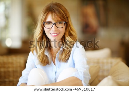 Close-up portrait of beautiful happy woman looking at camera and smiling while sitting on sofa. Royalty-Free Stock Photo #469510817