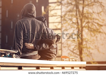 Portrait of cute couple with skateboards hugging over city town background 